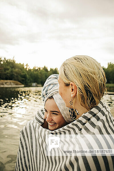 Young female friends wearing towel at lake during vacation