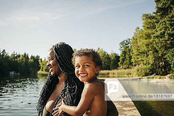 Smiling woman carrying excited son at lake during vacation
