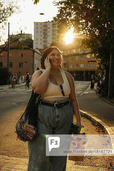 Glückliche üppige Frau  die mit ihrem Smartphone telefoniert  während sie bei Sonnenuntergang auf der Straße steht
