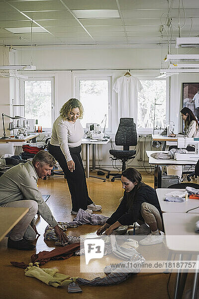 Eine Modedesignerin hilft ihren Kollegen beim Sortieren von recycelten Kleidungsstücken auf dem Boden einer Werkstatt