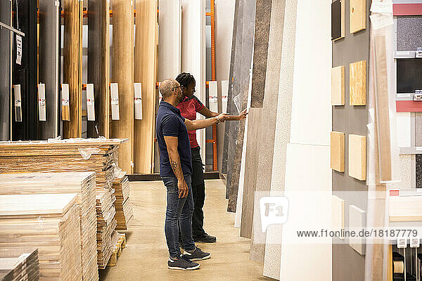 Side view of male customer with saleswoman choosing laminated boards at hardware store