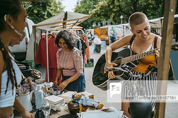 Lächelnde Kundin spielt Gitarre beim Einkaufen auf dem Flohmarkt
