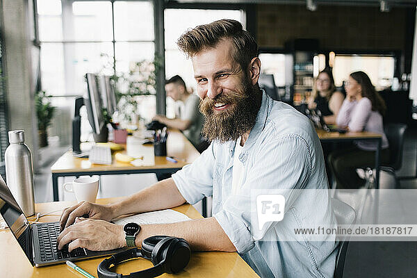 Porträt eines lächelnden männlichen Computerprogrammierers  der auf einem Laptop tippt  während er im Büro arbeitet