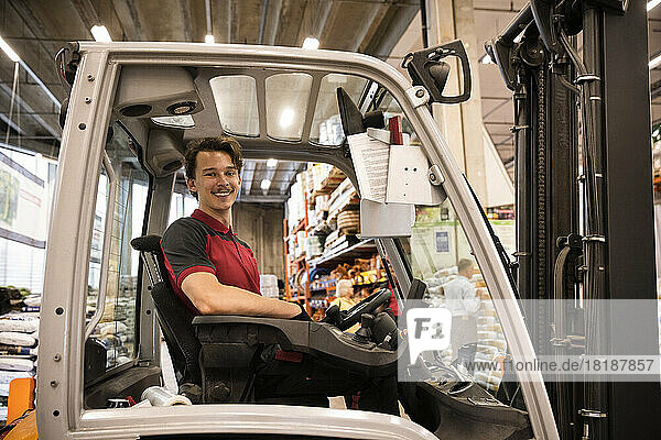 Smiling warehouse worker sitting in forklift at warehouse