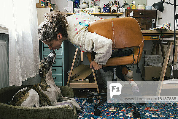 Frau küsst Hund  während sie auf einem Stuhl zu Hause sitzt