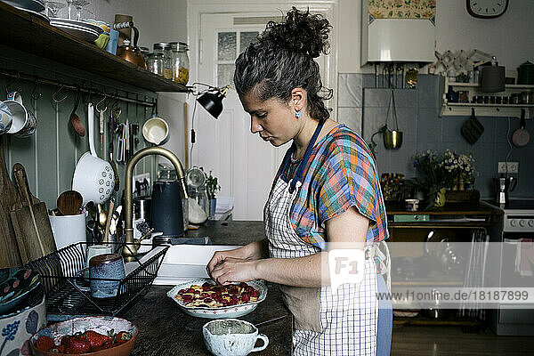 Seitenansicht einer Frau mit Schürze  die einen Kuchen garniert  während sie in der Küche steht