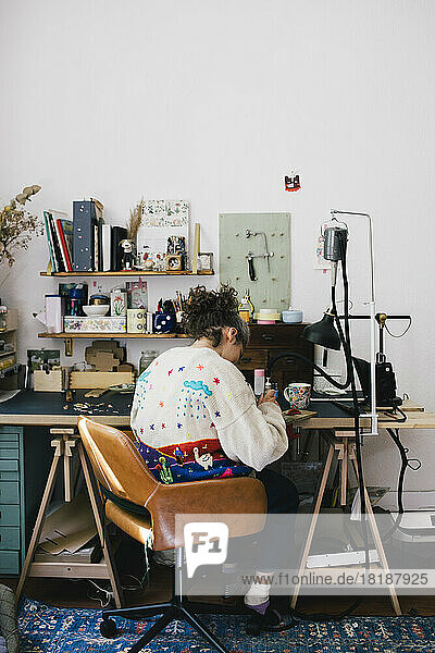 Schmuckherstellerin sitzt bei der Arbeit zu Hause auf einem Stuhl