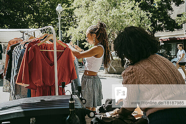 Seitenansicht einer Kundin  die beim Einkaufen auf einem Flohmarkt ein Kleid in ein Regal hängt