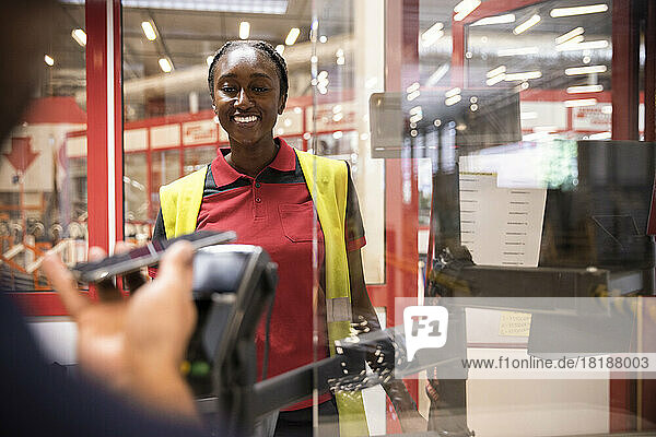 Lächelndes weibliches Verkaufspersonal betrachtet den Kunden  der an der Kasse online bezahlt