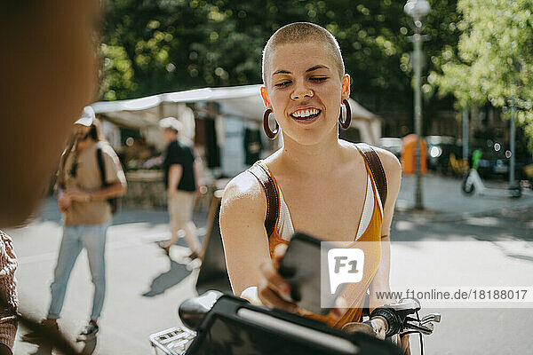 Lächelnde Frau mit rasiertem Kopf  die beim Einkaufen auf dem Flohmarkt mit dem Wasserhahn bezahlt