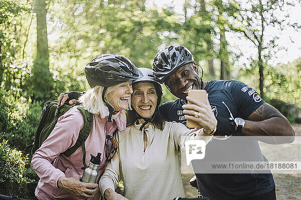 Smiling senior woman taking selfie through smart phone with male and female friend