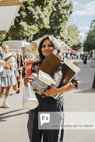Porträt einer lächelnden Frau  die verschiedene Waren auf einem Flohmarkt in der Hand hält