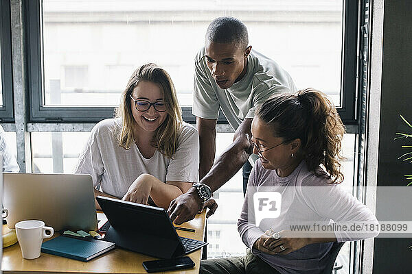 Lächelnde multirassische weibliche und männliche Computerprogrammierer  die über einem Laptop im Büro diskutieren