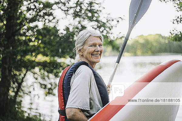 Portrait of happy senior woman holding paddleboard and oar