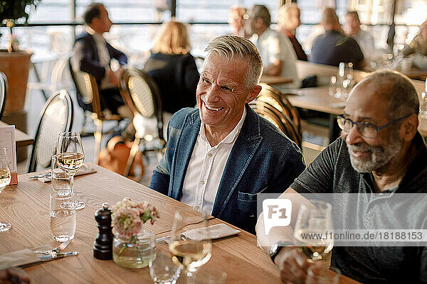 Happy senior man sitting by male friend in restaurant