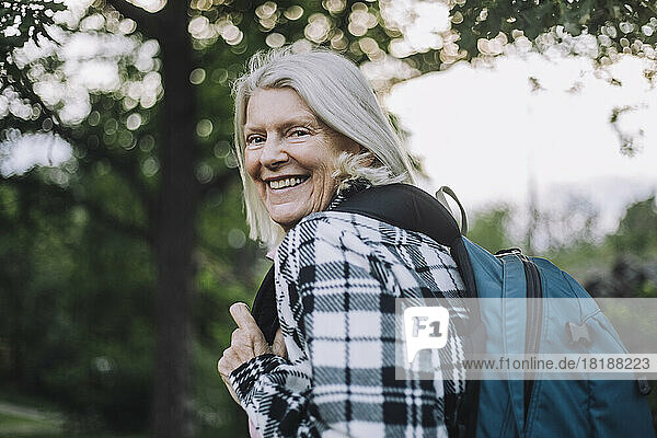 Porträt einer glücklichen älteren Frau  die beim Wandern einen Rucksack über die Schulter trägt