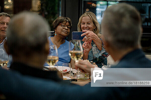 Lächelnde ältere Frauen fotografieren männliche Freunde mit Weingläsern in einem Restaurant