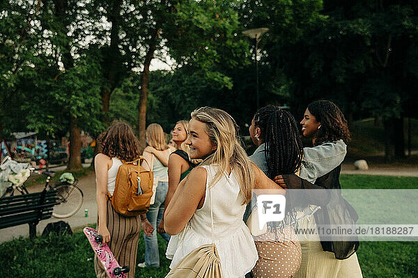 Lächelndes blondes Teenager-Mädchen geht mit Freundinnen im Park spazieren