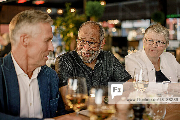 Smiling senior man talking with male friend while sitting by woman in restaurant