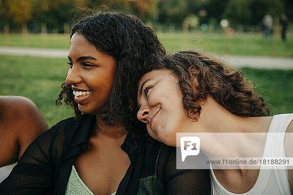 Lächelndes Teenager-Mädchen lehnt sich im Park an die Schulter eines Freundes