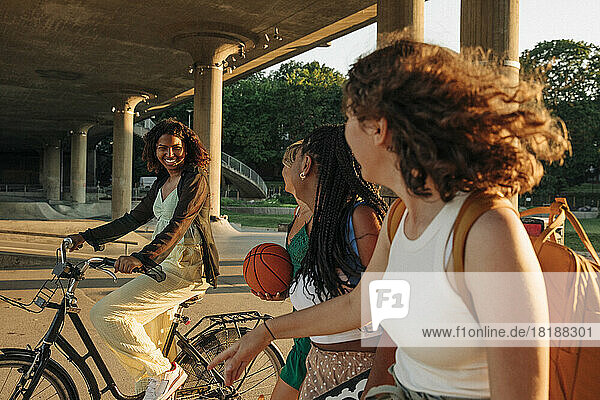 Teenager-Mädchen  die eine lächelnde Freundin betrachten  die unter einer Brücke Fahrrad fährt