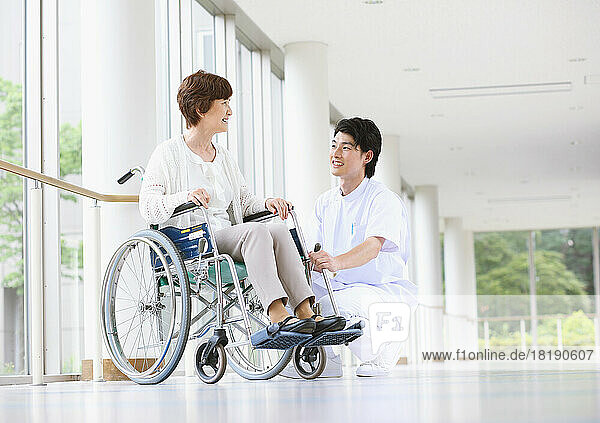 Senior Japanese woman in a wheelchair and a young male nurse having a conversation in the hallway