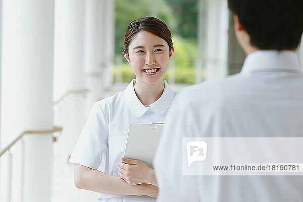 Smiling young Japanese female nurse having a conversation in the hallway