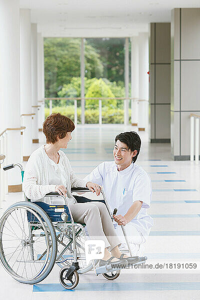 Japanese senior woman in a wheelchair and a young male nurse conversing in the hallway