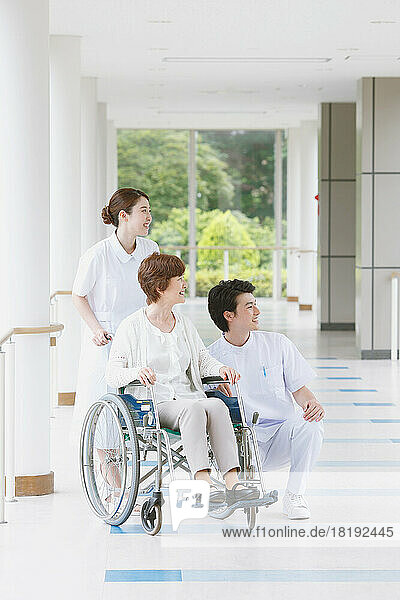 Japanese senior woman in wheelchair and two young nurses in the hallway