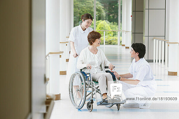 Japanese senior woman in a wheelchair and a two young nurses having a conversation in the hallway