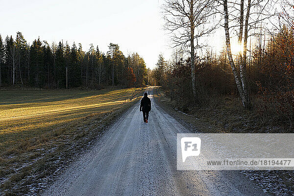 Woman walking on rural road at sunset