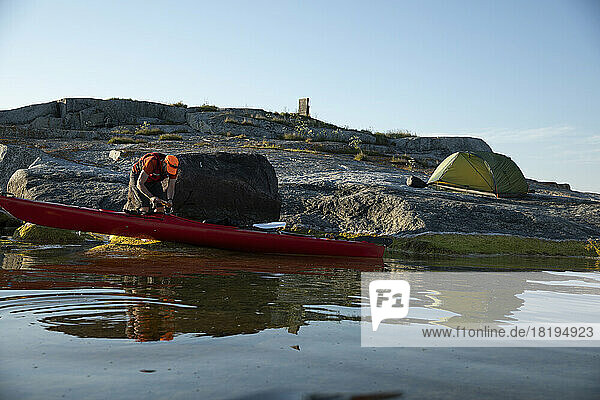 Man with kayak camping on coastal rocks