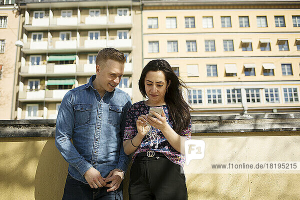 Woman showing man her smartphone on balcony