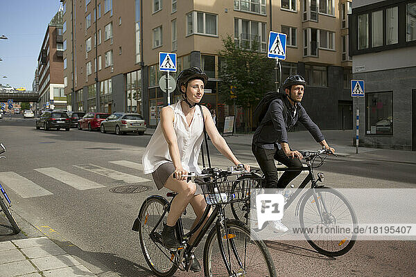 Young man and woman riding bicycles on city street