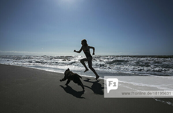 Mädchen und Haustier Hund läuft auf sonnigen Ozean Strand
