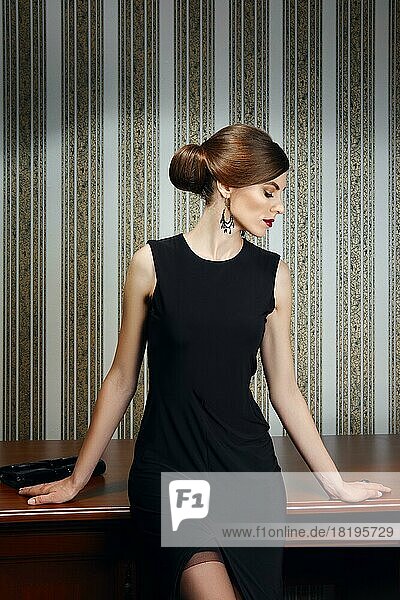 Wunderschöne Dame im eleganten schwarzen Abendkleid lehnt sich an den Tisch und schaut zur Seite