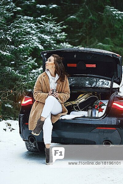 Eine müde Autofahrerin hält ihr Auto auf einem winterlichen Waldweg an  um sich auszuruhen und eine Tasse Kaffee zu trinken