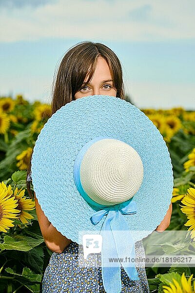 Positive junge Frau versteckt sich mit blauem breitkrempigem Hut