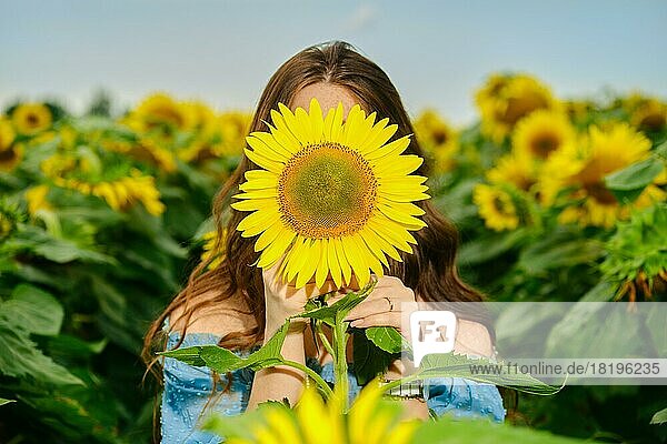 Junge Frau versteckt ihr Gesicht mit einer Sonnenblume