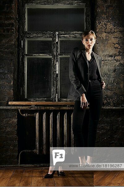 Stilvolle junge Frau  die in einem dunklen Raum in der Nähe des Fensters balanciert. Low key full length portrait