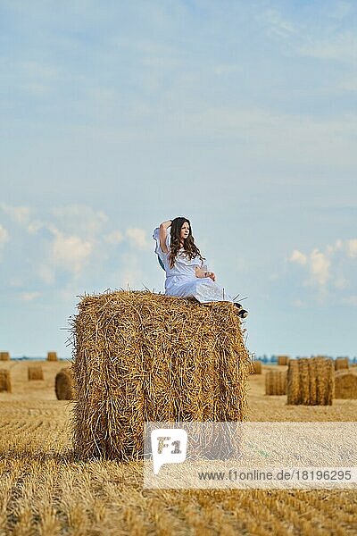 Verträumte junge Frau sitzt oben auf einem Strohhaufen auf dem Feld