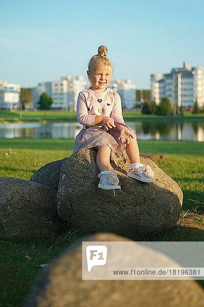 Niedliches kleines Kind sitzt auf Stein in Sonnenuntergang Zeit
