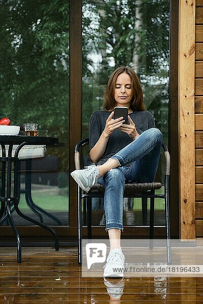 Woman checking what is online sitting on terrace of wooden cabin