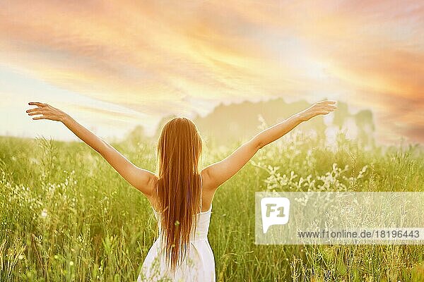 Junge Frau  die ihre Hände seitlich ausbreitet und der Sonne zugewandt auf einem Feld steht
