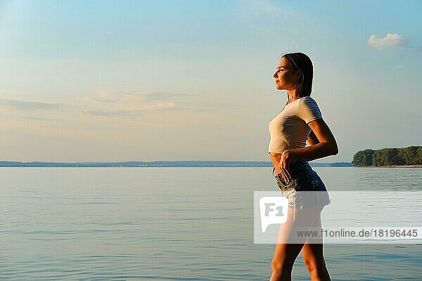 Schöne junge Frau genießt die frische Abendluft am See bei Sonnenuntergang