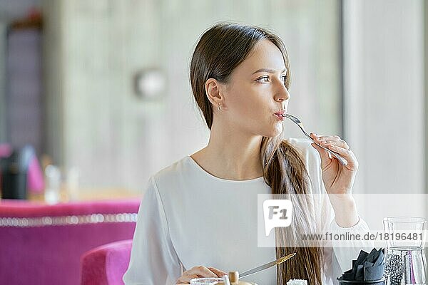 Junge Frau sitzt in einem Café  isst in der Pause Kuchen und schaut aus dem Fenster