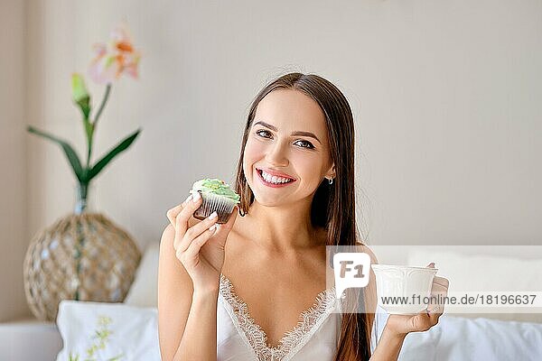 Süßes Mädchen isst Kuchen und trinkt Tee im Bett