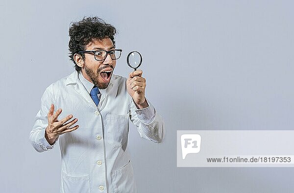 Überraschender Wissenschaftler  der mit einem Vergrößerungsglas zur Seite schaut. Wissenschaftler hält ein Vergrößerungsglas und schaut zur Seite  Mann im weißen Kittel mit Vergrößerungsglas schaut Werbung