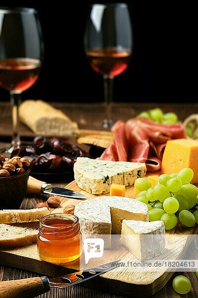 Käseteller mit Prosciutto  Weintrauben  Honig  Datteln  Crackern und Wein auf einem hölzernen Hintergrund