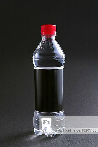 Plastikflasche Wasser mit schwarzem Etikett und rotem Deckel auf dem Tisch